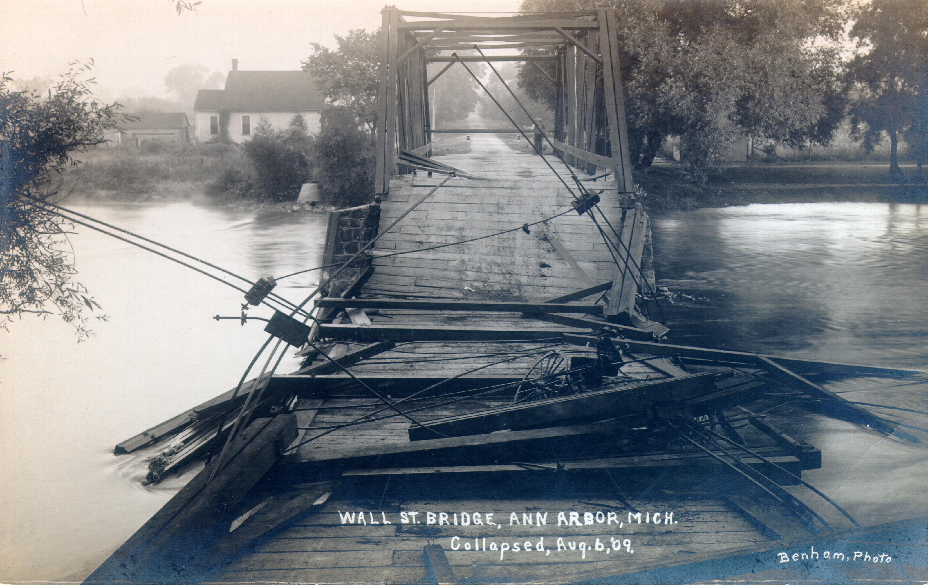 Collapsed Wall Street Bridge with broken decking in the foreground, the far span still upright, and a small house across the river on the left.